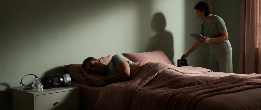 man asleep in bed, beside sleep apnea treatment adjustment equipment.