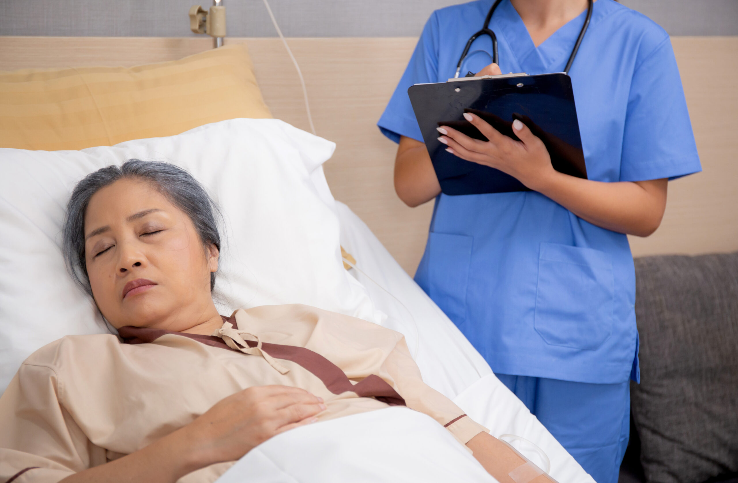 Asian nurse check saline and check patient elderly while asleep on bed at hospital ward, doctor diagnostic senior woman while sleep and writing report on clipboard, medical and insurance concept.